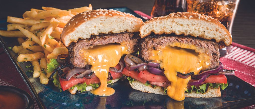 A juicy 'Juicy Lucy' burger with molten cheese oozing from the center, served on a bun with fresh lettuce, tomato, and a side of crispy French fries.