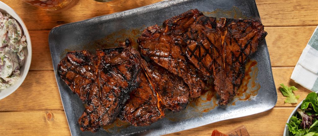 Perfectly grilled T-bone steaks with a shiny barbecue glaze, served with grilled vegetables on the side.