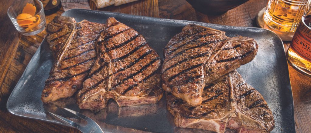 Juicy T-bone steaks grilled to perfection, showcasing a rich bourbon marinade, served with a side of grilled vegetables.
