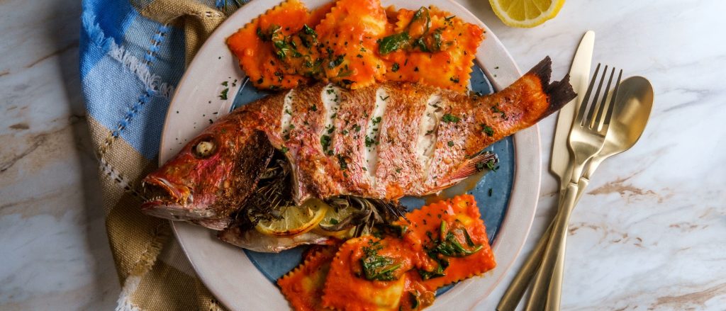Grilled whole red snapper stuffed with lemon, garlic, and oregano, topped with a fresh olive, pepper, and feta salad.