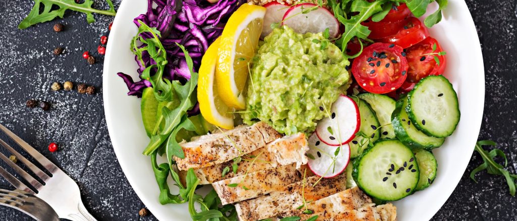 Lunch bowl with grilled chicken, quinoa, tomato, guacamole, red cabbage, and cucumber.