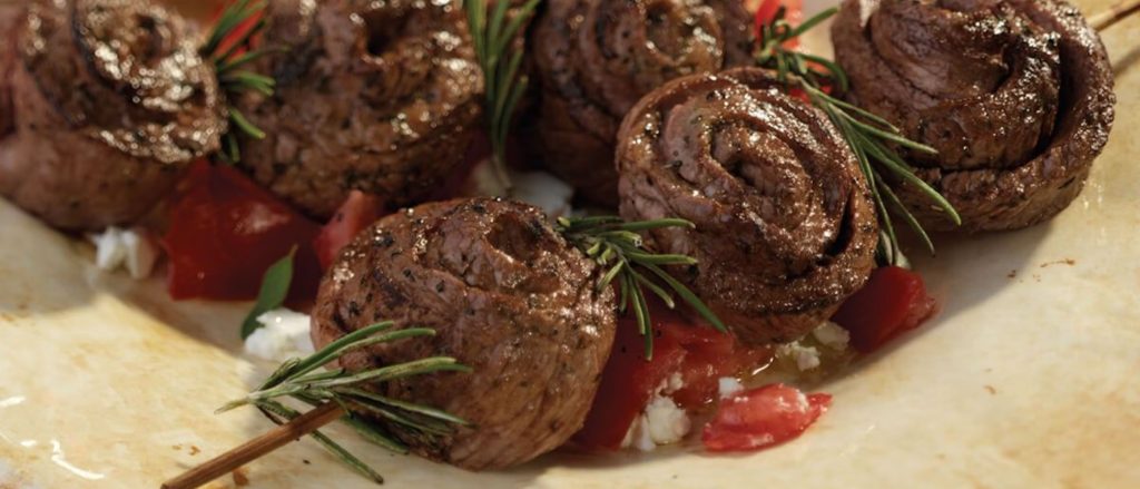 Grilled steak pinwheels on skewers with tomato salad.
